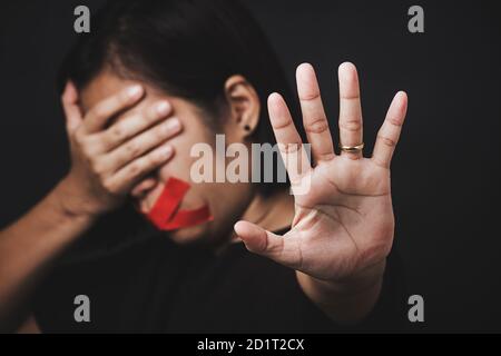 Donna bendata avvolgente bocca con nastro adesivo rosso e mostrare segno di mano smettere di abusare di violenza e abuso su sfondo nero, tratta di esseri umani e ab Foto Stock