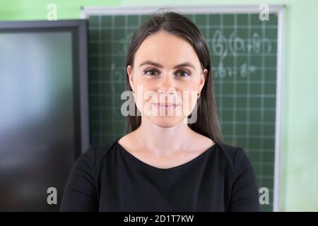 Primo piano di una giovane insegnante di sesso femminile vicino a lavagna e digitale schermo in aula Foto Stock