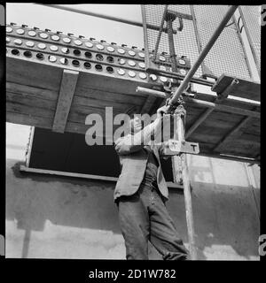 Un uomo che assembla ponteggi durante la costruzione del Penhill Estate, Penhill, Swindon, Wiltshire, UK. Foto Stock