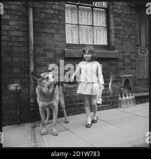 Una giovane ragazza e un cane alsaziano in piedi sul marciapiede fuori di una casa a schiera, Middleport, Burslem, Stoke-on-Trent, Staffordshire, Regno Unito. Foto Stock