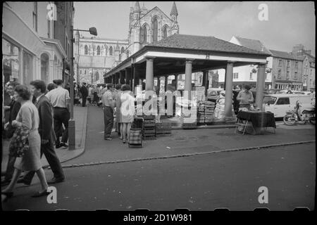 Vista generale della Piazza del mercato, che mostra gli Shambles, un mercato coperto eretto nel 1766, con venditori e acquirenti in primo piano, e l'elevazione est della Chiesa del Priorato di Sant'Andrea sullo sfondo. Foto Stock