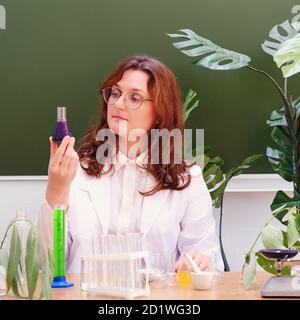 L'insegnante di sesso femminile esamina la reazione chimica di un reagente in un matraccio. Esperimenti scientifici in una classe di chimica scolastica Foto Stock