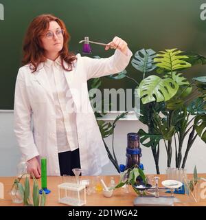 Donna ecologa con matraccio chimico e imbuto per liquido in mano. Analisi, test e ricerca nel laboratorio scolastico Foto Stock