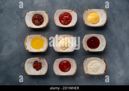 Diverse salse gustose in ciotole, varie salse su fondo di pietra grigia, vista dall'alto Foto Stock