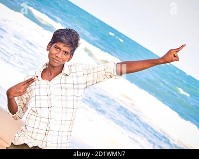 PUDUCHERRY, INDIA - DICEMBRE CIRCA, 2018. Teenager indiano non identificato che alza il braccio in trionfo al mare. Giovane ragazzo nero in piedi sulla spiaggia e showin Foto Stock