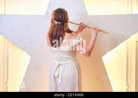 La musicista femminile suona il flauto vicino alla stella incandescente, vista dal retro Foto Stock