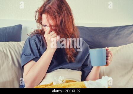 Ragazza rossa soffia il naso in una sciarpa sdraiata il letto con una tazza di tè Foto Stock