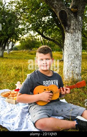 Chitarrista giovane ragazzo all'aperto. Boy on City Park estate prato godendo di una giornata a suonare la chitarra. Foto Stock