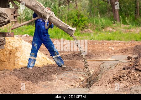 Lavoratore di costruzione che posa cemento o calcestruzzo nella cassaforma di fondazione. Costruzione di fondamenta di casa Foto Stock