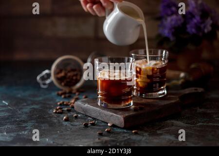 Caffè espresso un bicchiere, con latte, che viene versato dalla caraffa a mano. Bevanda rinfrescante estiva. Foto Stock