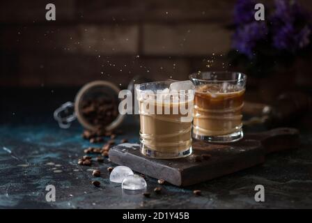 Spruzzare il caffè ghiacciato in un bicchiere e i chicchi di caffè su uno sfondo marrone. Bevanda rinfrescante estiva. Foto Stock