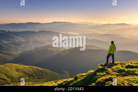 Uomo sportivo sulla cima della montagna che guarda sulla valle di montagna Foto Stock