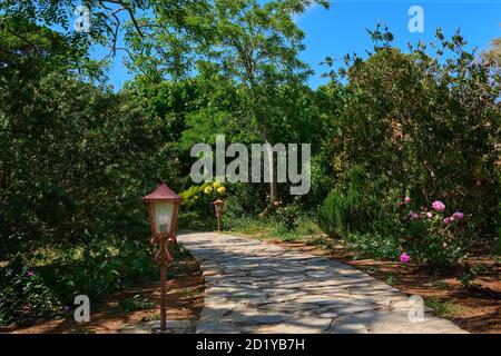 Idee di disegno di giardinaggio. Pavimentatrici naturali, sentieri, decorazioni, lanterne. Ricco fogliame, cespugli e alberi. Percorsi tortuosi, terreno aperto, nessun pacciame. Scatto diurno Foto Stock