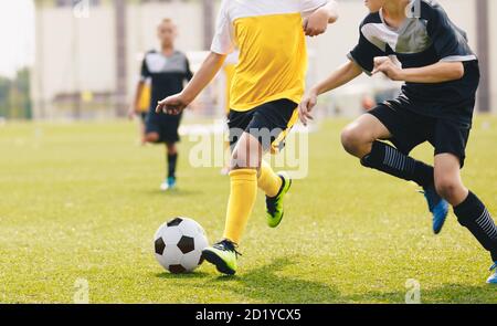 Bambino che calcia palla di calcio in un duello. I calciatori in corsa competono per la palla. Bambini che frequentano la partita di calcio della scuola Foto Stock