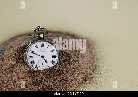 Vecchio orologio tascabile su cuscino nero e sfondo grigio testurizzato. numeri romani che indicano l'ora Foto Stock