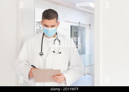 Giovane medico con maschera chirurgica di fronte a chirurgia prendere note - mettere a fuoco sul viso Foto Stock