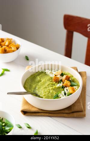 Salutare e delizioso brodo di purea di broccoli e crema di cetrioli con mozzarella, cipolle verdi e crostini, ciotola di zuppa su un tavolo bianco Foto Stock