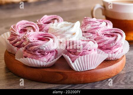 marshmallow rosa e bianco (zephyr) su tavola rotonda di legno con una tazza di caffè su sfondo grigio di legno Foto Stock