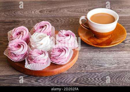 marshmallow rosa e bianco (zephyr) su tavola rotonda di legno con una tazza di caffè su sfondo grigio di legno Foto Stock