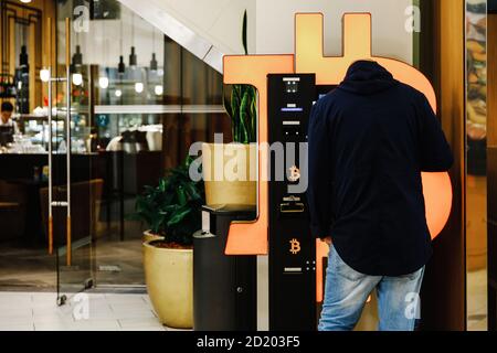 Riga, Lettonia - circa Ottobre, 2020: Uomo calvo utilizza Bitcoin ATM macchina in centro commerciale per lo scambio di criptovaluta Foto Stock