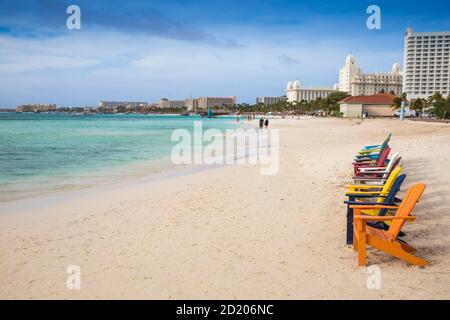 Aruba, una fila di colorate sedie a sdraio in legno su Palm Beach Foto Stock