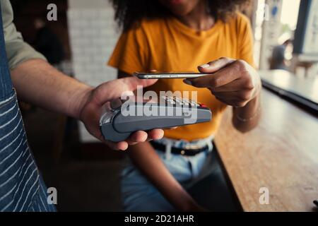 Donna afroamericana che scansiona il codice a barre della macchina della scheda con lo smartphone che paga il caffè nel funky caffè. Foto Stock