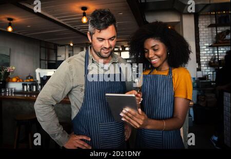 I proprietari di una caffetteria maschile e femminile sorridono al tablet nella caffetteria. Foto Stock