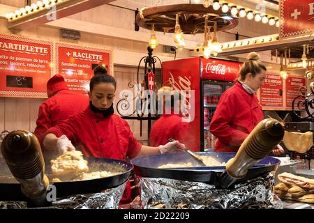 PARIGI, FRANCIA - 6 GENNAIO 2019: Giovane donna che prepara le tartiflette (formaggio fuso, patate e prosciutto a base di piatto) in grandi padelle alla cucina tradizionale della Savoia Foto Stock