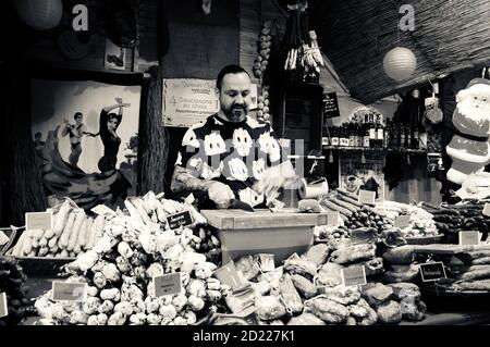 PARIGI, FRANCIA - 26 NOVEMBRE 2017: Macellaio giovane in divertente t-shirt che vende prosciutto tradizionale catalano e salsicce secche al mercato di Natale a la Defense Foto Stock