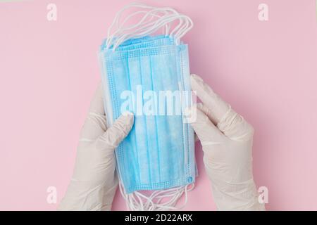 Vista superiore delle mani della donna in guanti di gomma bianca che tengono maschere mediche blu su sfondo rosa. Foto Stock