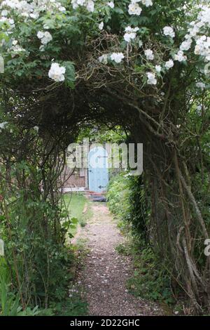 Vista sul paesaggio nel giardino estivo di campagna inglese con pera di espalier albero con frutta lavanda rosa arco fiori cespuglio erba prato & piante & porta segreta Foto Stock