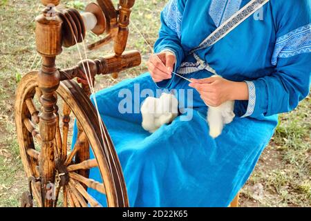 Una donna in un vestito blu che gira un mandrino. Ruota in legno retrò per la filiera. Foto Stock