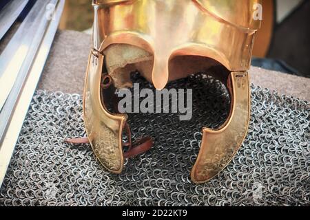 Antico vestito romano per una campagna militare. Casco giallo vintage giace sulla catena posta, primo piano. Casco in bronzo vero romano con fodera, stile di vita. Foto Stock