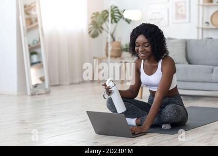 Bella donna africana che si esercita a casa, utilizzando il computer portatile Foto Stock