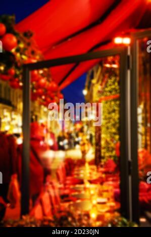 Foto sfocata della terrazza del caffè parigino decorata per Natale. Luci di strada serali. La gente con i sacchetti di shopping alla strada - regali d'acquisto. Foto Stock