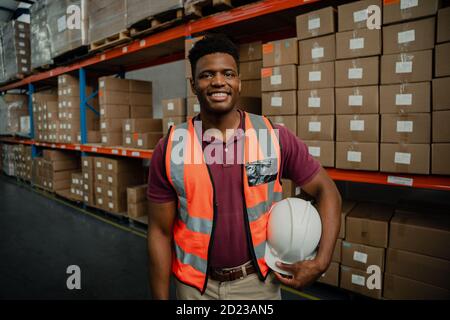 Bel maschio che tiene il hardhat che lavora in fabbrica negozio imballaggio pacchi per la consegna Foto Stock