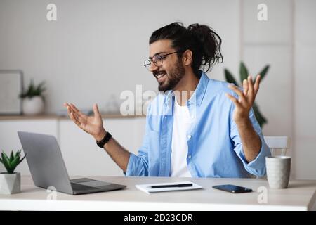 L'uomo indiano eccitato festeggia emotivamente il successo di affari con il computer portatile in ufficio Foto Stock