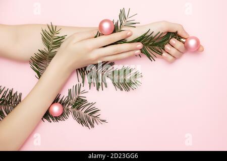Primo piano belle mani womans tenendo un ramo albero di Natale con palline rosa sullo sfondo rosa, con spazio di copia. Concetto di pubblicità delle unghie Foto Stock