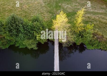 Vista aerea di un semplice ponte sospeso su un piccolo fiume. Paesaggio estivo, fiume con passerella, vista dall'alto. Ponte sospeso sul fiume Foto Stock