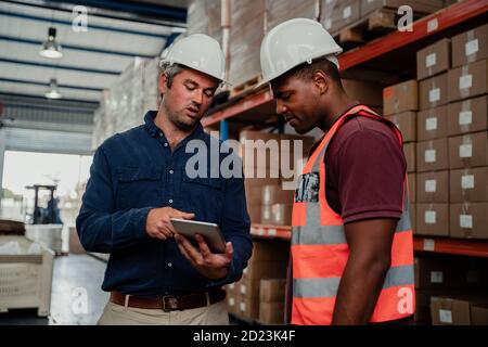 Supervisore caucasico che spiega suggerimenti per il miglioramento al lavoratore etnico in officina. Foto Stock