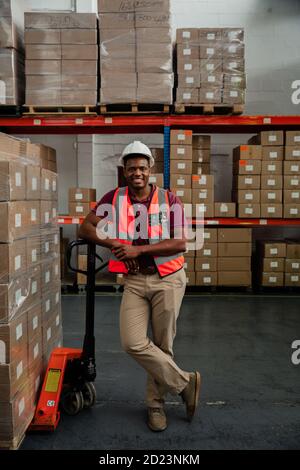 Lavoratore maschio a lunghezza intera sorridente appoggiandosi contro rimorchio di imballato pacchi in magazzino Foto Stock