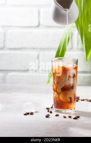 Caffè freddo estratto in una tazza di vetro alta e chicchi di caffè su fondo grigio in cemento. Versare il latte in un bicchiere di caffè. Foto Stock