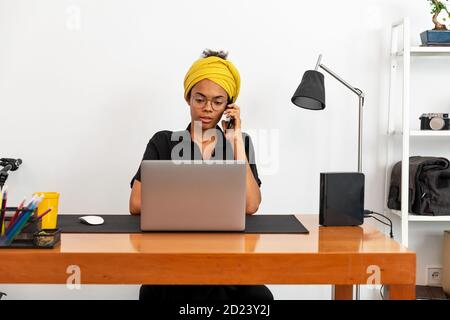 Foto di giovane donna latina che lavora in ufficio con portatile che parla sul telefono cellulare Foto Stock