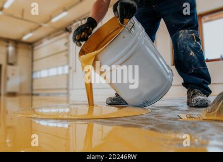 Operatore che applica un secchio di resina epossidica giallo sul pavimento. Foto Stock