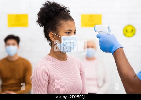 Il lavoratore medico che fa lo screening della temperatura per la ragazza del paziente in clinica, Foto Stock