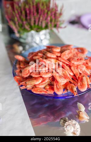 ULSTEINVIK, NORVEGIA - 2014 AGOSTO 23. Cotti i gamberetti freschi in una ciotola sul tavolo con la pianta sullo sfondo. Foto Stock