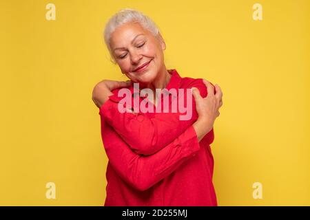 Donna che indossa abiti rossi che si abbracciano essendo positiva, sorridente fiducioso. Foto Stock
