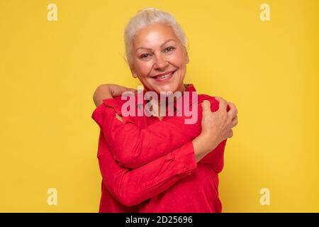Donna che indossa abiti rossi che si abbracciano essendo positiva, sorridente fiducioso. Foto Stock