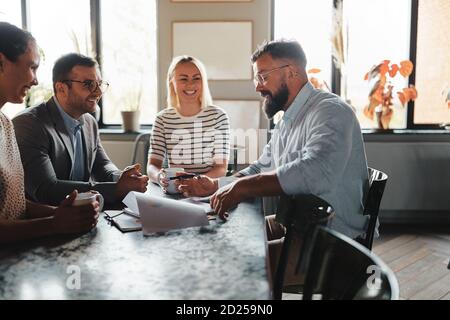 Gruppo di uomini d'affari che ride mentre si riuniscono per un incontro informale sopra il caffè nell'area salotto di un ufficio