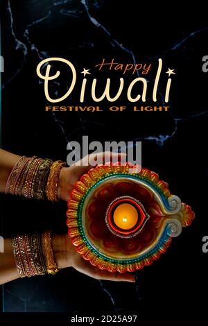 Happy Diwali - Donna mani con hennè che tiene accesa candela isolato su sfondo scuro. Lampade Clay Diya illuminate durante Dipavali, festa indù delle luci ce Foto Stock